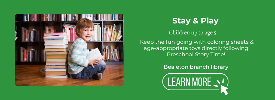 young boy holding an open book in front of bookshelves. Stay and Play following Preschool Story Time, Bealeton branch library
