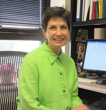 Smiling woman in green shirt at a desk with computer and background.